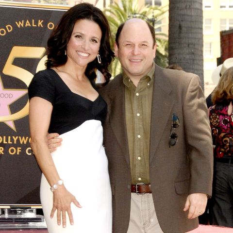 Jason Alexander in a brown coat poses a picture with wife Title.